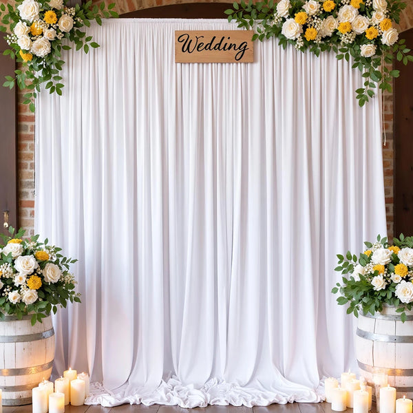 A white satin backdrop curtain decorated with floral garlands and candles for a wedding or photography event.