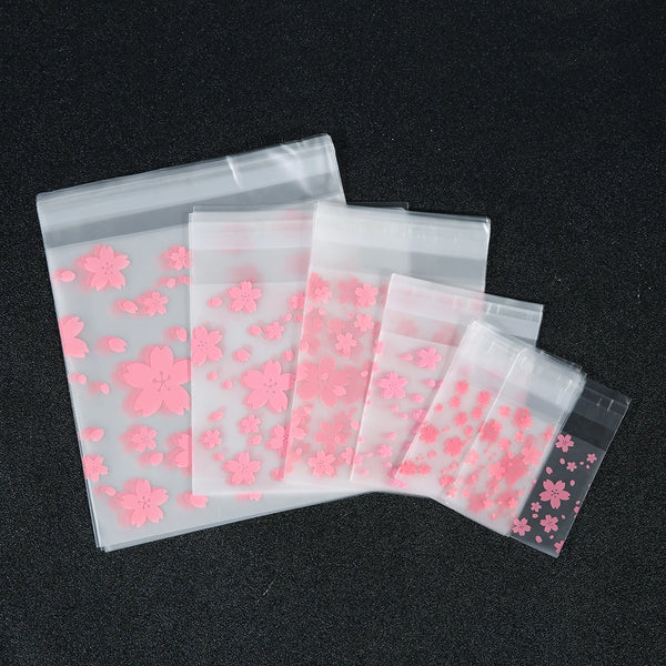 A collection of pink cherry blossom self-adhesive storage pouches arranged diagonally on a dark surface.