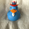 A blue rubber duck toy wearing a red hat with stars and an orange beak, resting on a silver-colored surface.