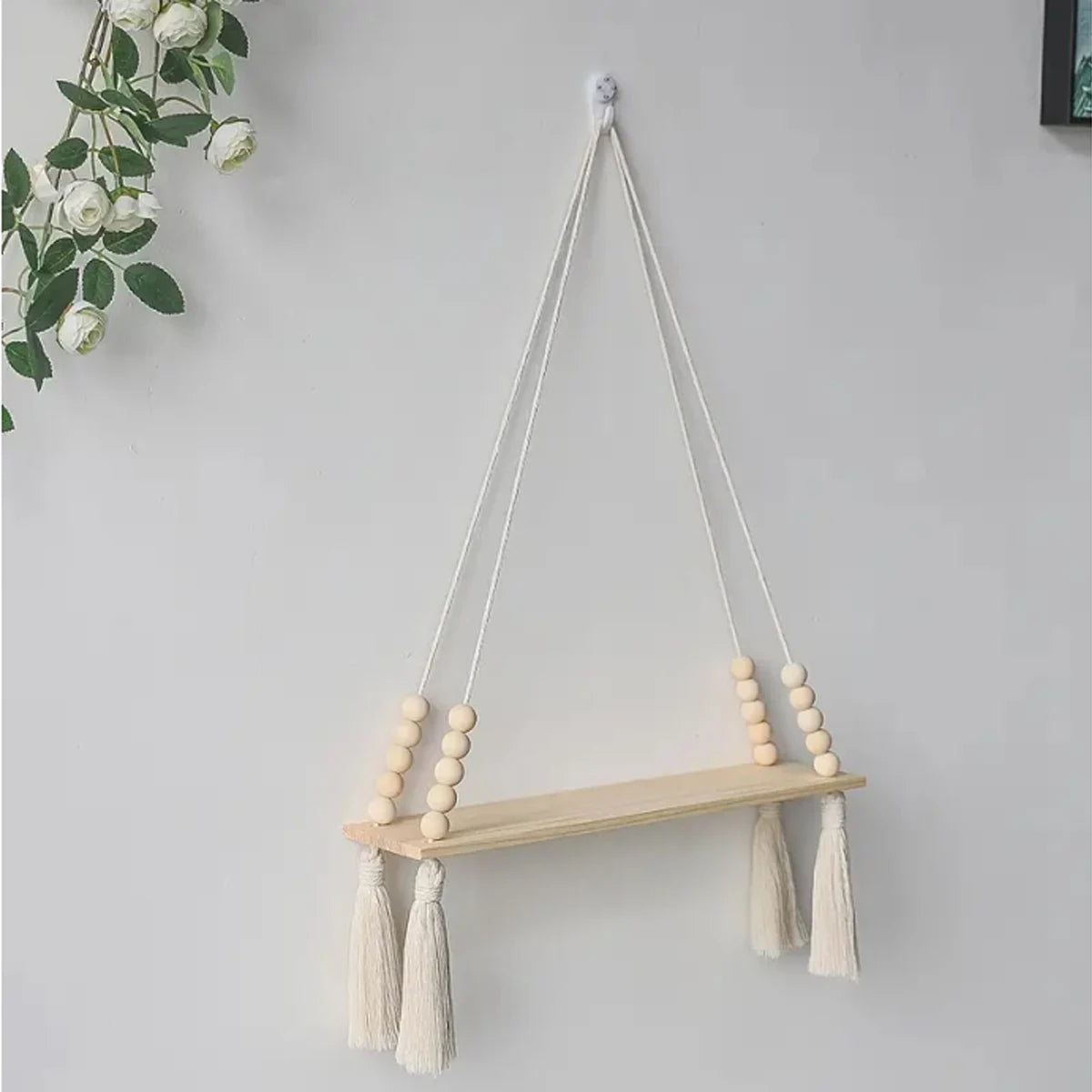 Handmade macrame wood wall shelf with tassels hanging on a white wall.