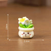 A small white resin charm shaped like a potted yellow and white flower with a cute face, displayed on a wooden surface.