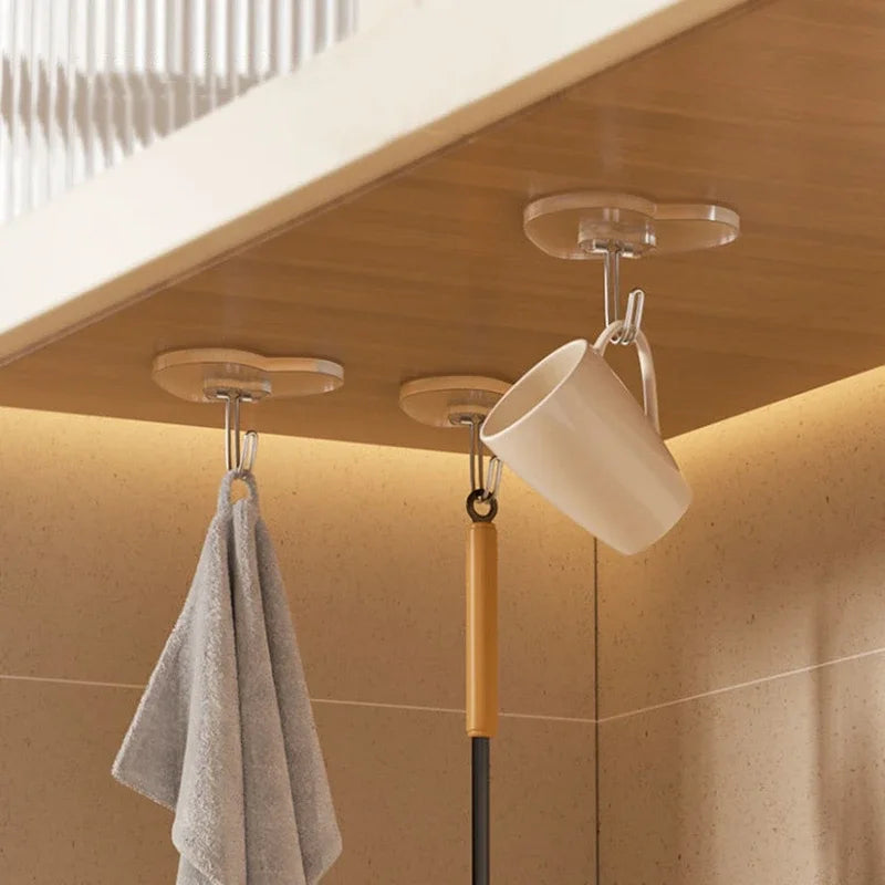 A set of transparent self-adhesive hooks is shown hanging from a ceiling fixture above a towel rack.