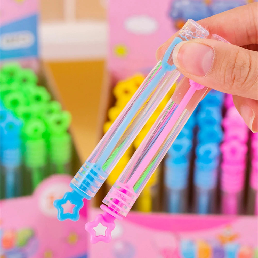 Une main tient deux tubes de bulles en plastique transparent avec des pointes colorées, emballés dans une boîte rose.