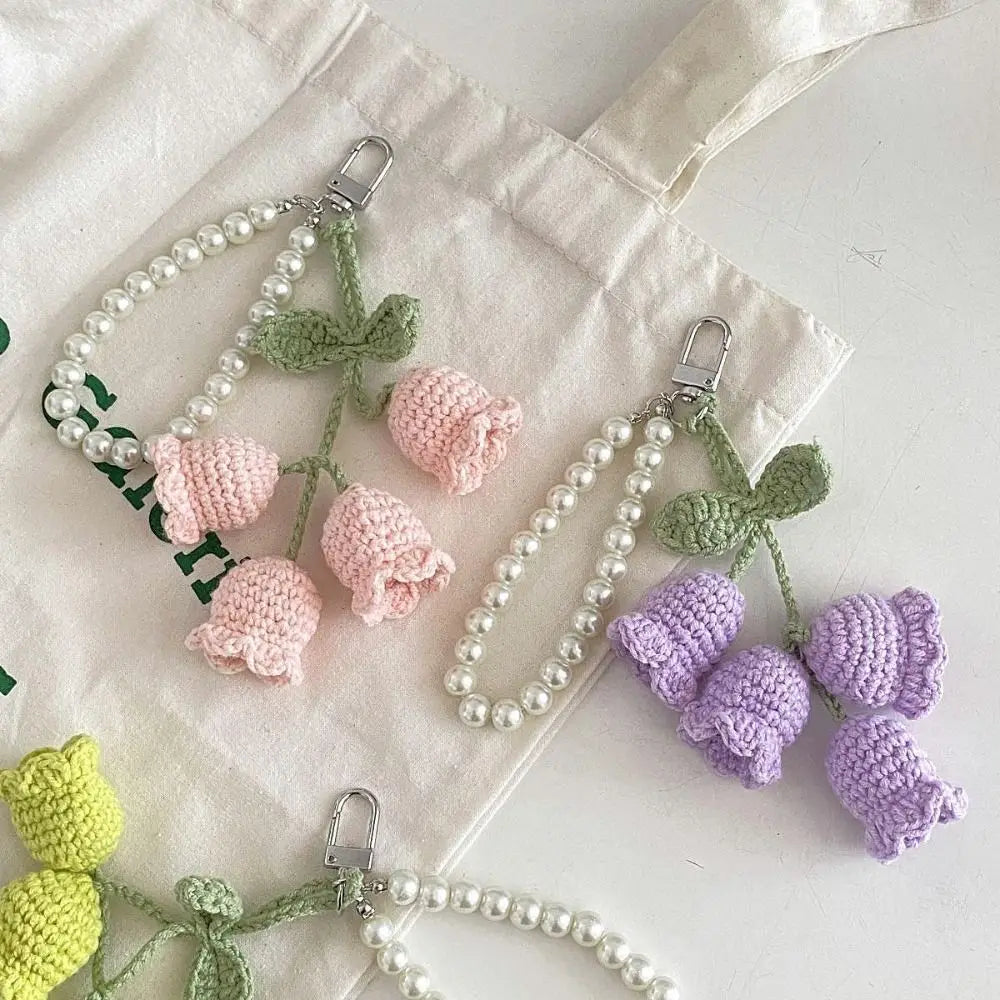 Handmade pearl chain orchid key rings with green and purple floral charms displayed on a white cloth bag.