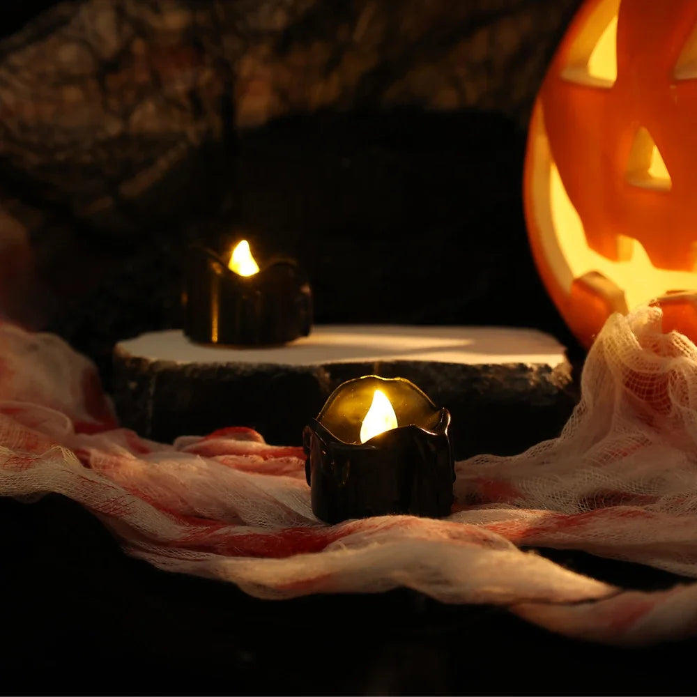 A dark, moody photograph featuring several black LED candles with a warm white glow resting on a white surface draped with sh