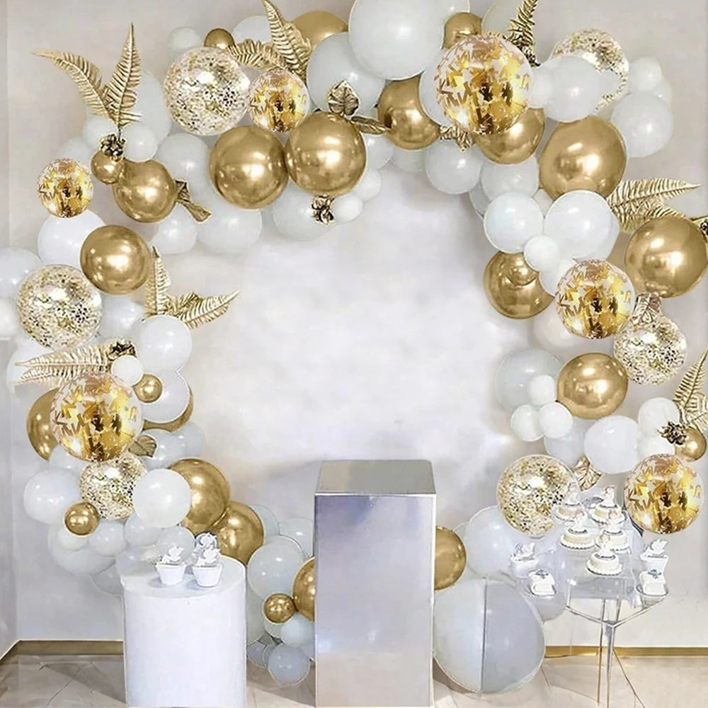 An archway decorated with white and gold confetti balloons and metallic silver columns.