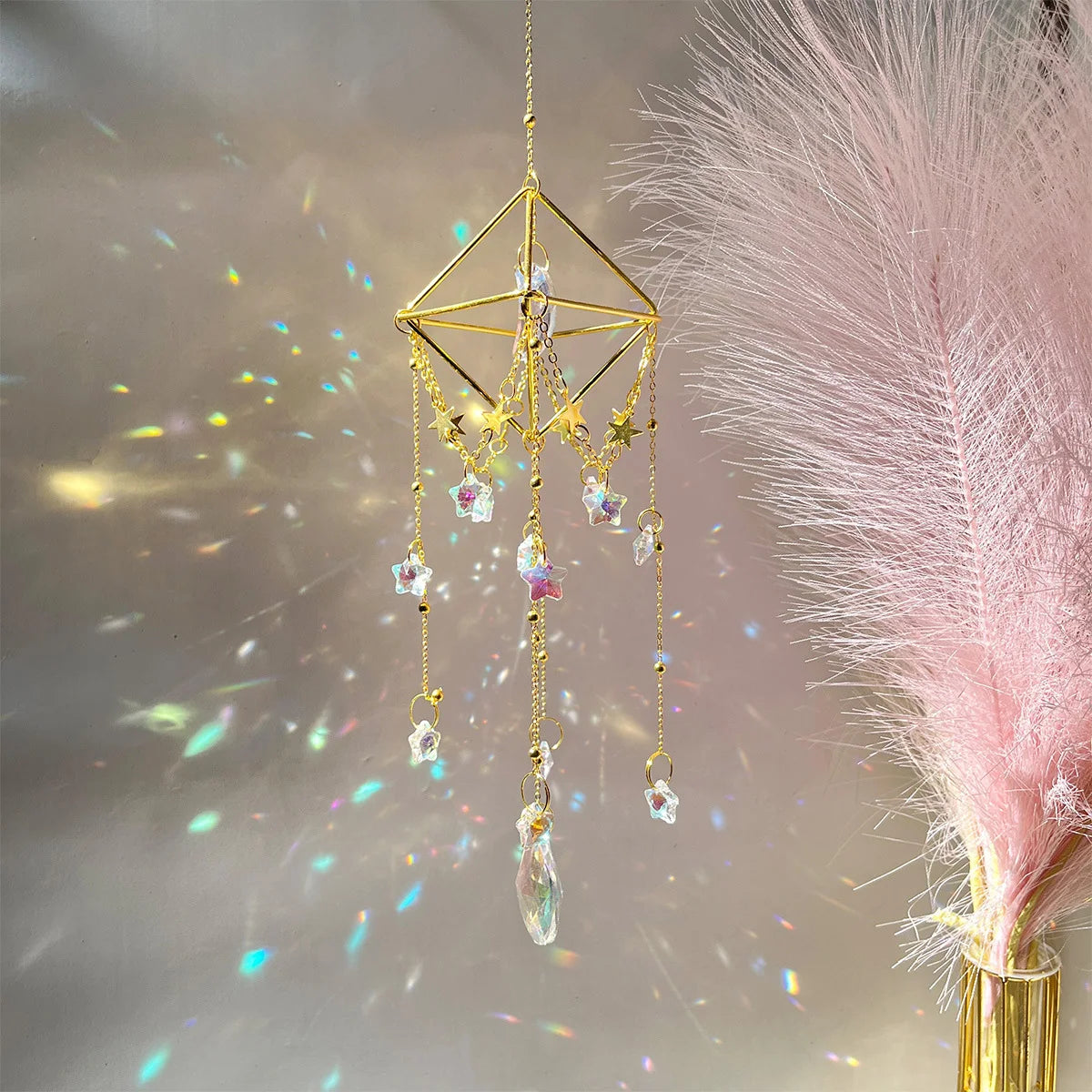 A gold crystal hanging suncatcher decoration with multiple dangling clear and pink crystals against a soft, glowing backgroun