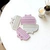 A set of pink and white cat food bag squeezers or no-waste dispensing tools resting on a white table next to a candle.