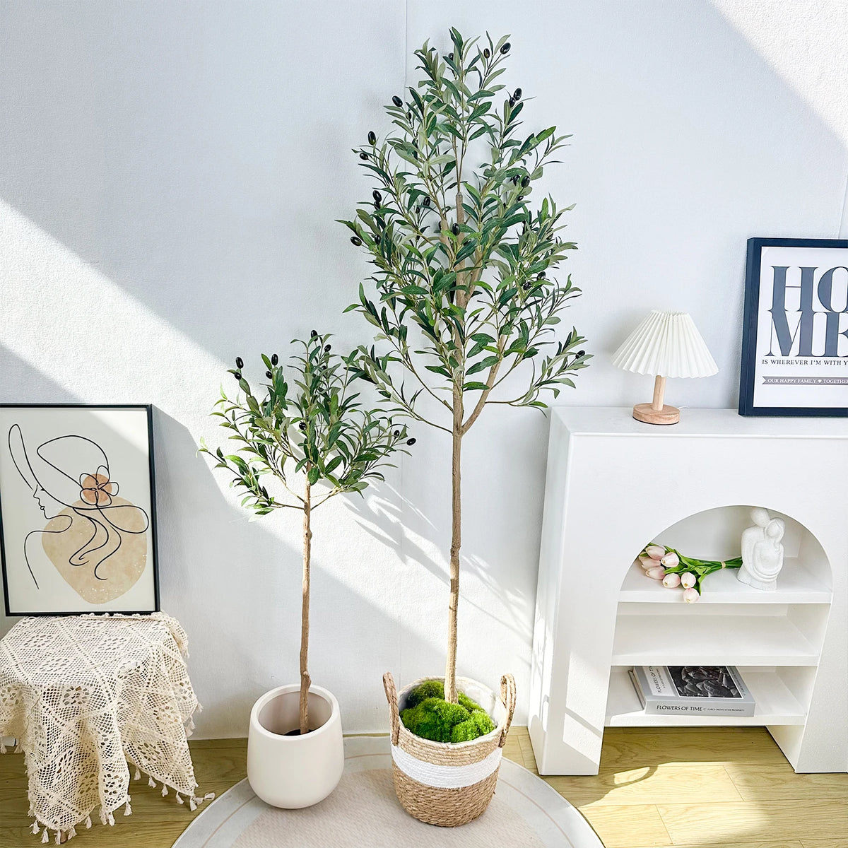 A tall artificial olive tree in a pot stands next to a white shelf with decorative items.