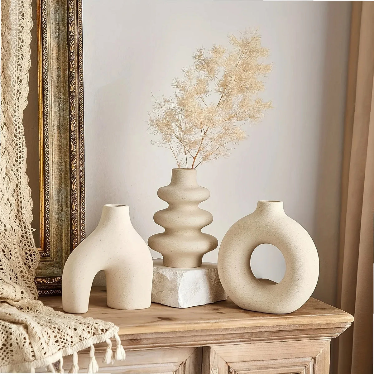 A set of three beige ceramic vases and a dried floral arrangement displayed on a wooden surface.