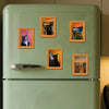 A light green refrigerator decorated with several framed pictures of black cats.