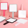 Pink and white compact handheld makeup mirrors displayed on a pink surface.