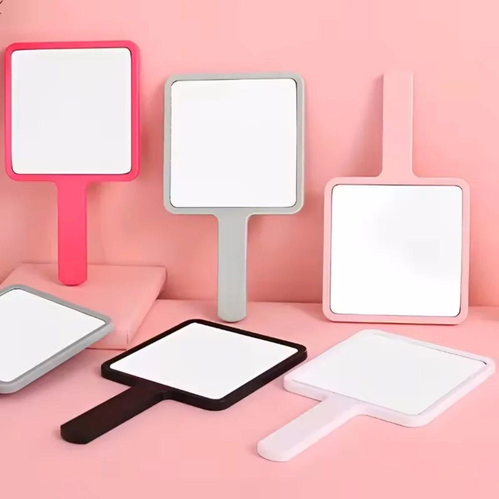 Pink and white compact handheld makeup mirrors displayed on a pink surface.