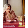 A close-up of a gold candle warmer lamp with a glass jar and wooden base resting on a red surface.