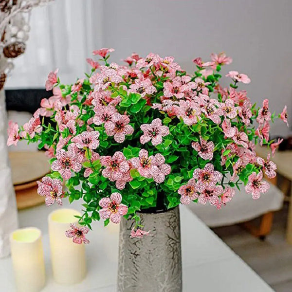 A bouquet of pink and green silk eucalyptus and violet artificial flowers in a gray vase.