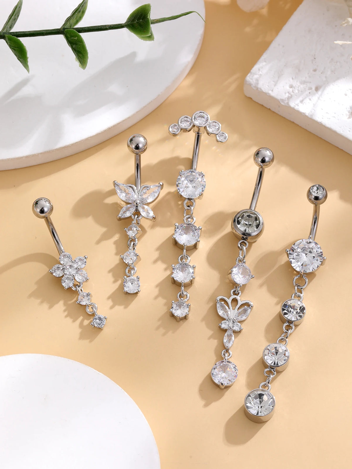 A set of five gold tone butterfly and flower belly rings displayed on a light beige surface.