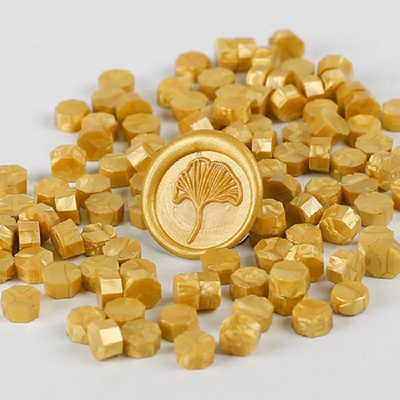 A pile of small, round, gold-colored wax sealing beads with a tree design stamp in the center.