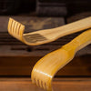 A light brown bamboo back scratcher with a roller massager is shown resting on a wooden surface.