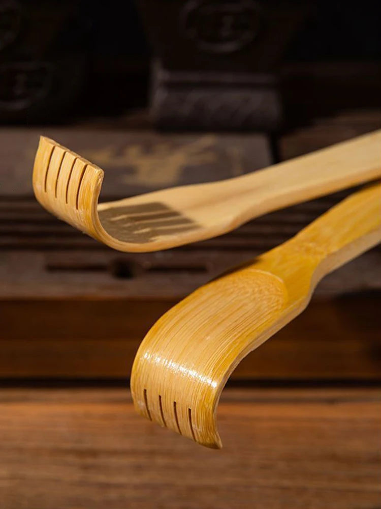 A light brown bamboo back scratcher with a roller massager is shown resting on a wooden surface.
