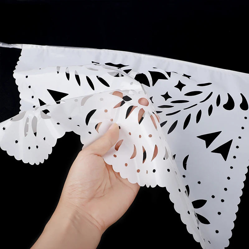 Eine Hand hält ein weißes Papelpicado-Banner mit kunstvollen ausgeschnittenen Designs für Partydekoration.