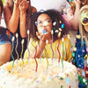 A person is blowing out candles on a birthday cake with many colorful lights and confetti in the background.