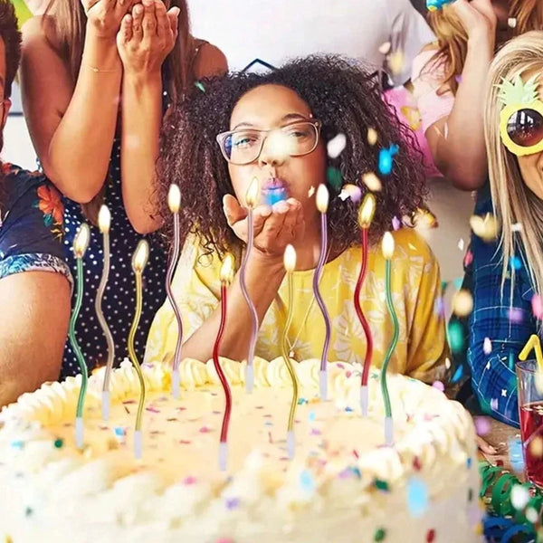 A person is blowing out candles on a birthday cake with many colorful lights and confetti in the background.