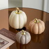 A set of three ceramic pumpkin figurines in pale beige and blush tones with gold accents displayed on a dark wooden surface.
