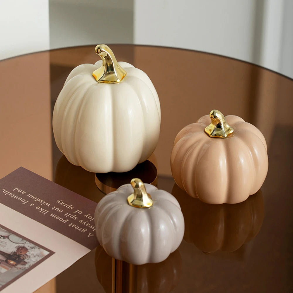 A set of three ceramic pumpkin figurines in pale beige and blush tones with gold accents displayed on a dark wooden surface.