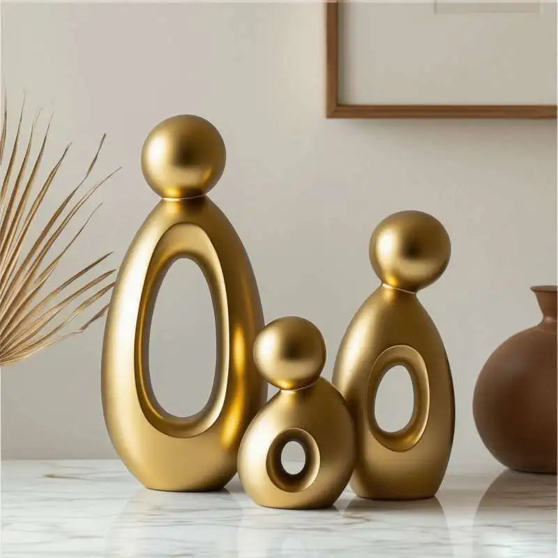 A set of three modern resin family statues in gold finish standing on a white marble surface.