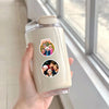 A hand holds a clear plastic bottle containing a sticker pack featuring the Golden Girls characters for DIY decoration.