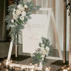 A wedding arch display featuring white and dusty rose flowers and silvery-green eucalyptus greenery.