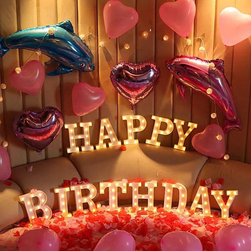 A birthday display featuring pink and purple heart-shaped balloons and warm white LED alphabet letters.