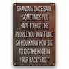 A dark metal wall sign with white text featuring a quote about hugging people you dislike.