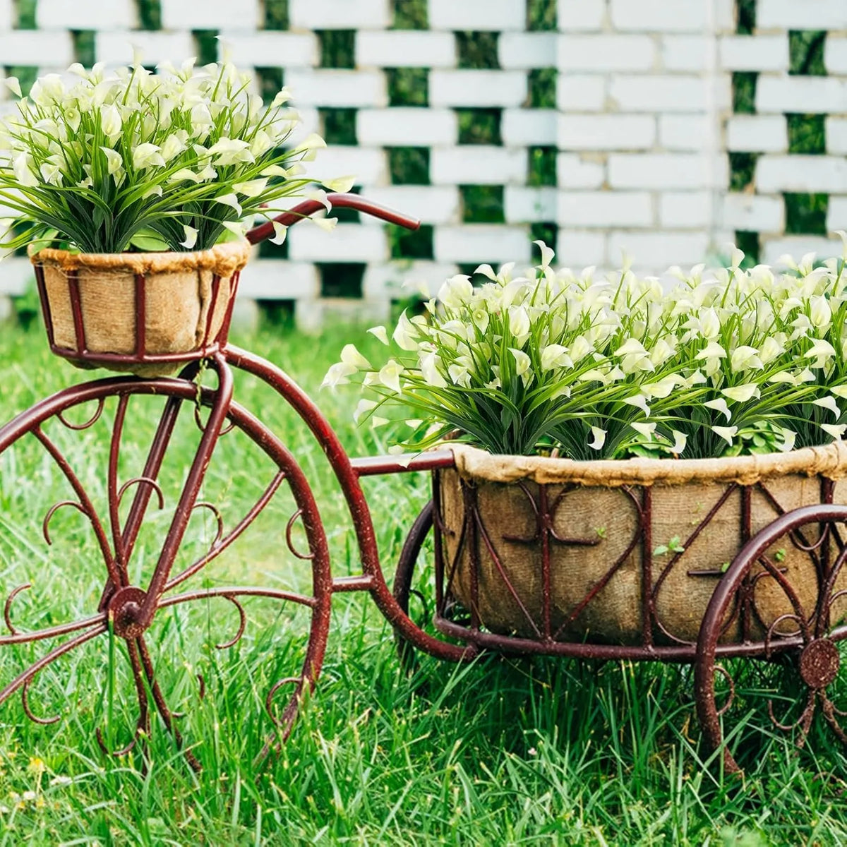 A vintage bicycle decorated with potted artificial calla lily bouquets in a grassy outdoor setting.
