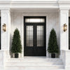 A pair of tall artificial cedar topiary trees flanking a white marble entryway with a black door.