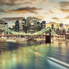 A nighttime view of the New York City skyline featuring illuminated skyscrapers and a large suspension bridge over the water.