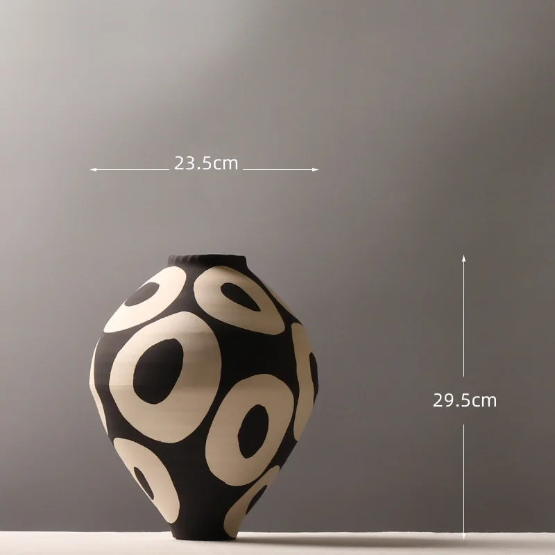 A black and cream ceramic vase with a geometric circle pattern displayed against a gray wall.