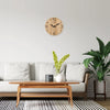 A wooden wall clock with a natural grain features black hands mounted on a light gray wall above a modern sofa.