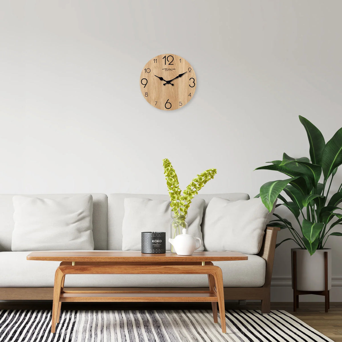 A wooden wall clock with a natural grain features black hands mounted on a light gray wall above a modern sofa.