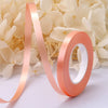 Roll of peach satin balloon ribbon unwinding against a background of white flowers.