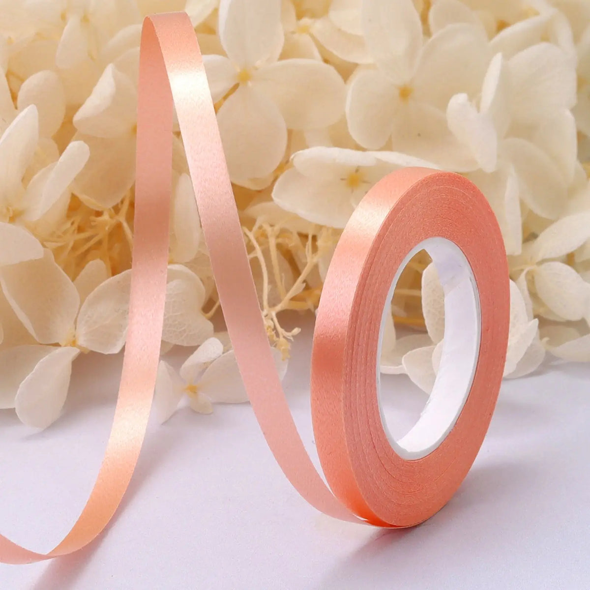 Roll of peach satin balloon ribbon unwinding against a background of white flowers.