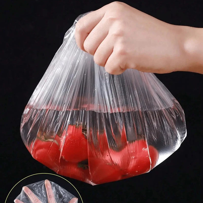 A hand is placing red tomatoes into a clear reusable elastic food cover bag.