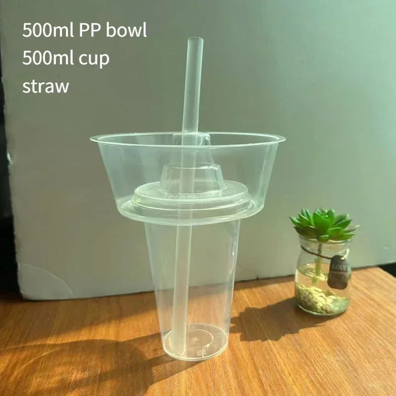 A clear plastic 500ml PP bowl with a straw is shown on a wooden surface.