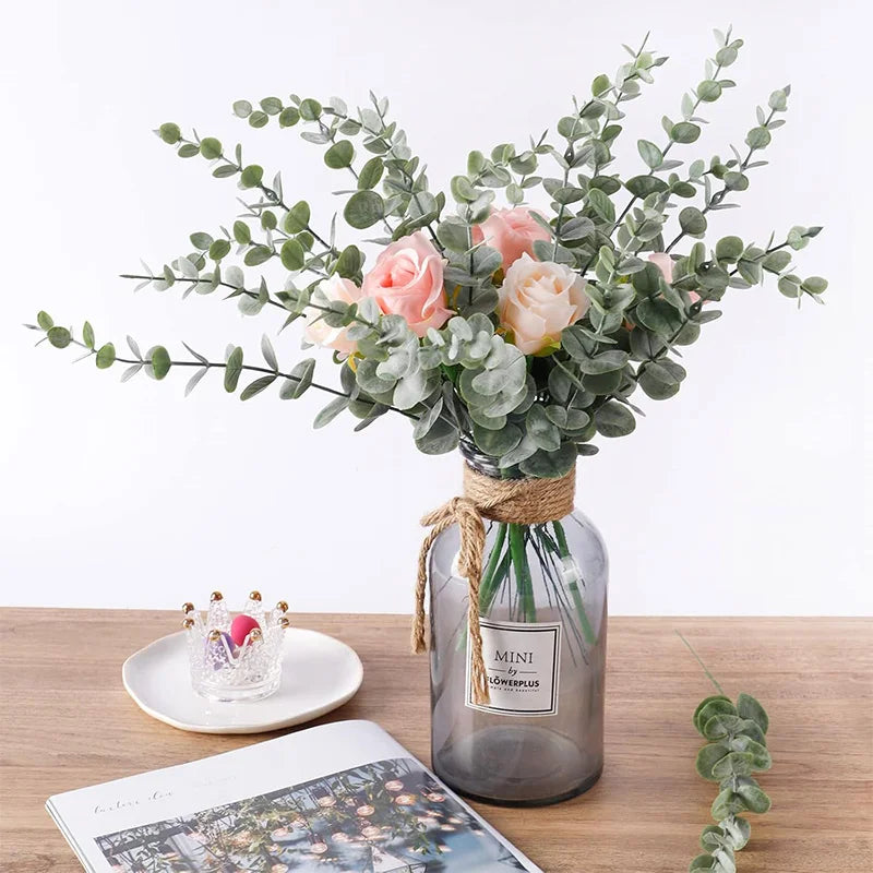 A bouquet of pink roses and green eucalyptus leaves arranged in a glass jar for home decor.