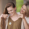 A woman is helping another woman put on an openable book pendant necklace.
