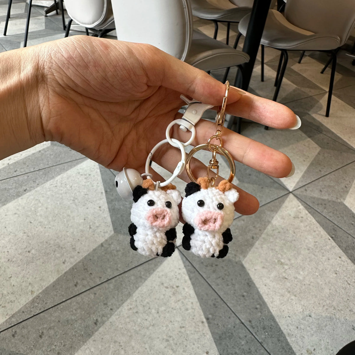 A hand holds a handmade crochet cow keychain featuring white and black wool figures.