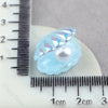 A translucent light blue mermaid cake topper featuring a pearl and seashell design, measured against a ruler.