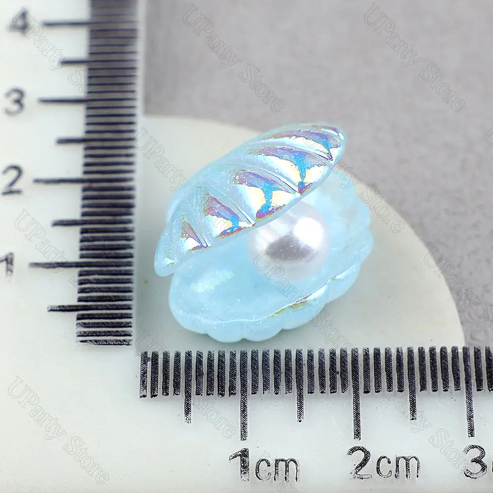 A translucent light blue mermaid cake topper featuring a pearl and seashell design, measured against a ruler.