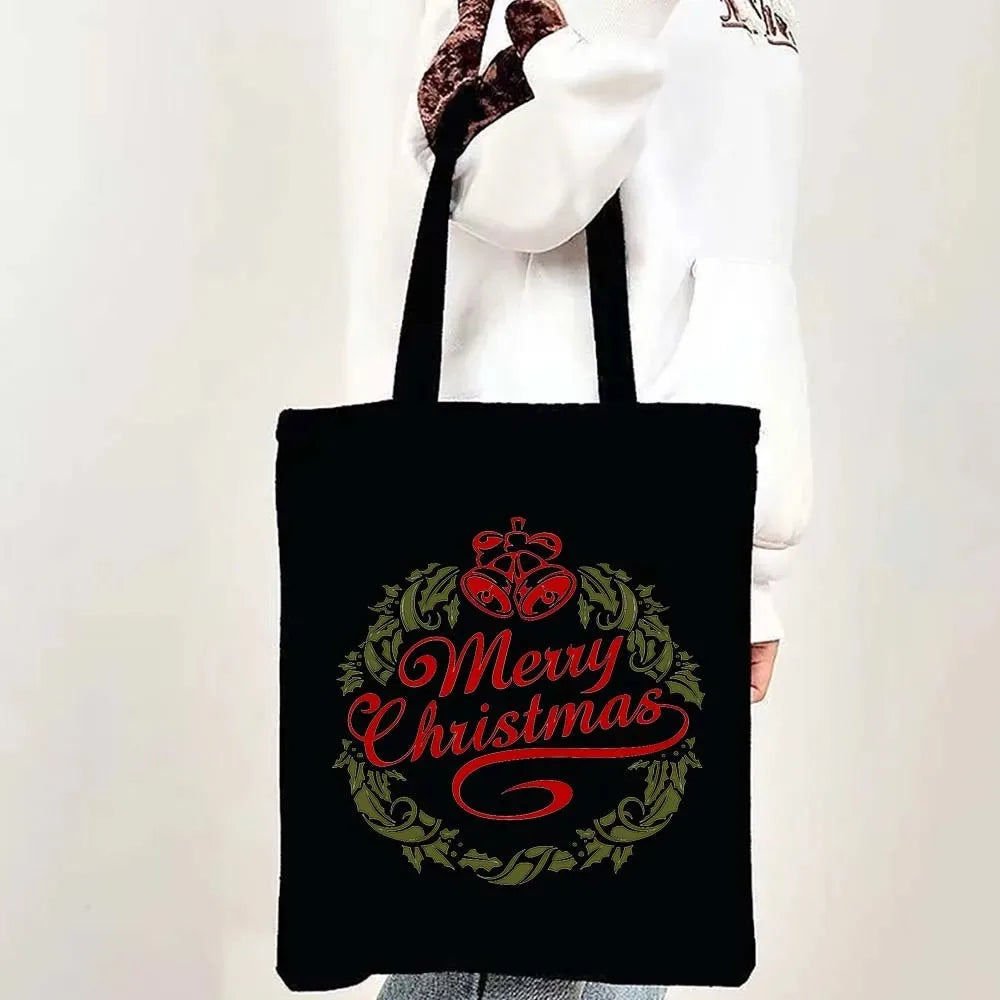 Black tote bag featuring a festive Christmas design with 'Merry Christmas' written in red script surrounded by green foliage.