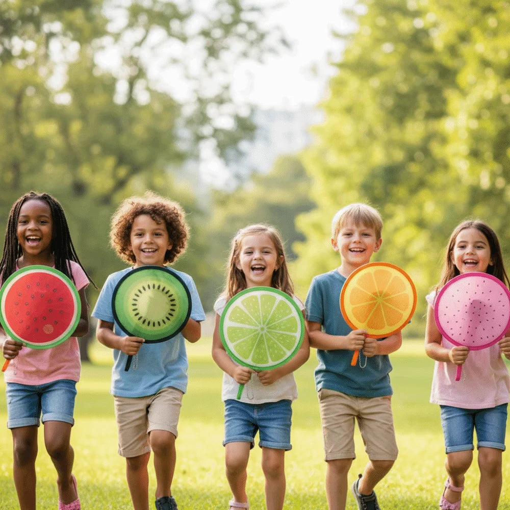Five children smiling outdoors holding colorful foldable hand fans with fruit designs